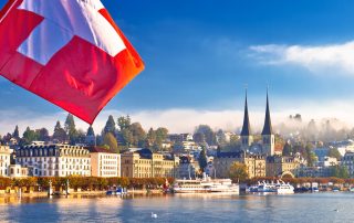 Schweizer Flagge vor Stadtansicht mit See und Kirchtürmen.